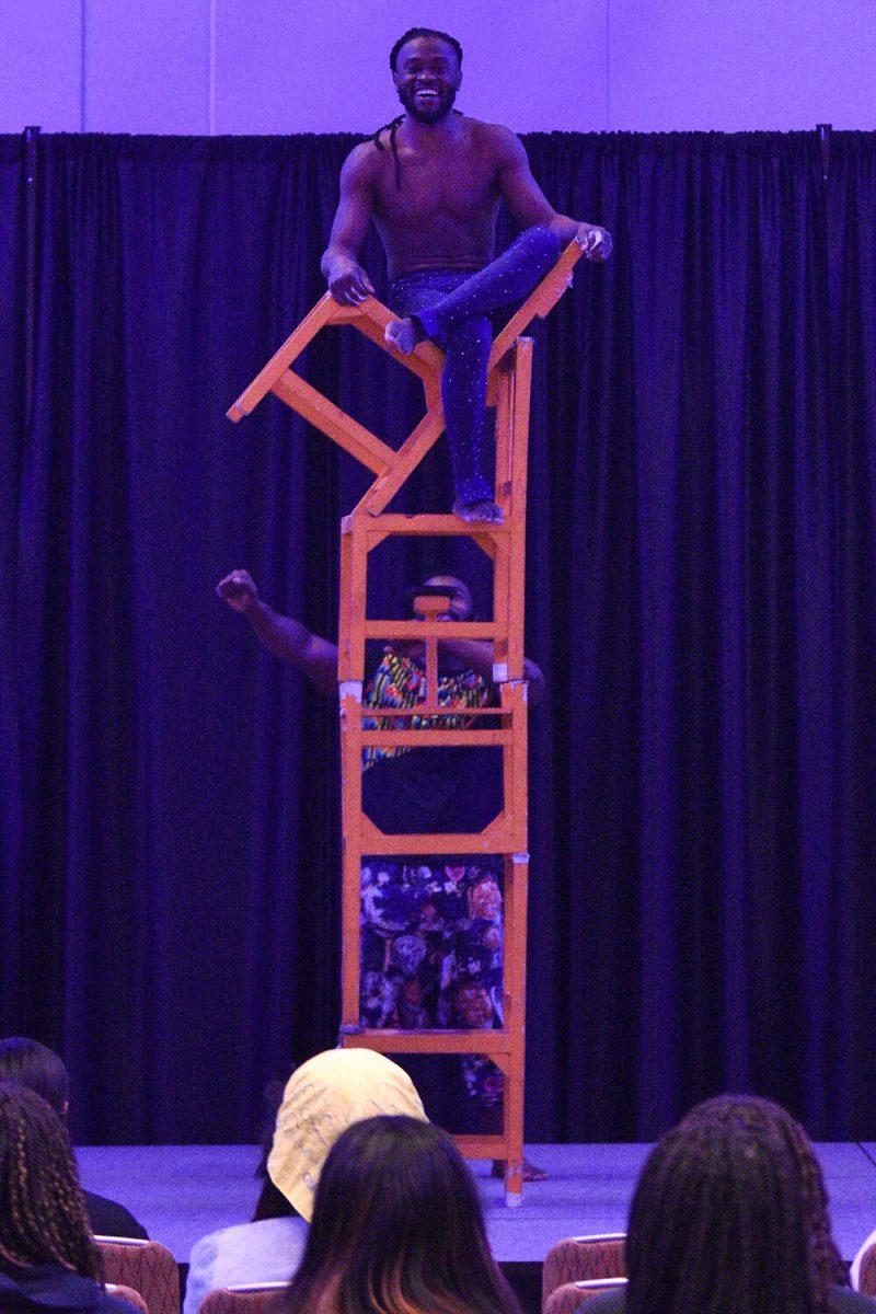 An acrobat sits atop four stacked chairs and smiles in the Piedmont-Mountain Ballroom in Talley Student Union on Wednesday, Feb. 8, 2023. The Zuzu Acrobats perform stunts for an audience.