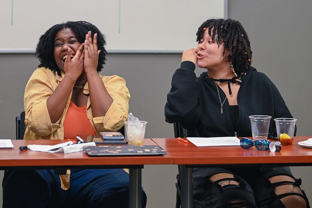 Mya McDowell (left), a fourth-year studying biology, covering her face and laughing while Sol Johnson (right), a fourth-year studying psychology, speaks in the African American Cultural Center on Wednesday, Feb. 15, 2023. At the Black History Month Chat n' Chew students discussed several poems about the black experience.