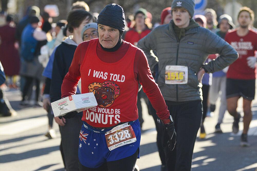 Non-challenger Ken Hayman runs past the Krispy Kreme Challenge finish line with a half-dozen box of donuts in hands on Hillsborough Street on Saturday, Feb. 4 2023. Ken was one of the 2,878 non-challengers to partake in the challenge.