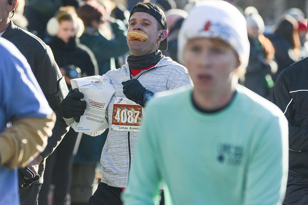 Non-challenger Nicholas Banister sprints past the finish Krisly Kreme Challenge finish line with a donut in his mouth at Hillsborough Street on Saturday, Feb. 4 2023. Many runners chose to eat the donuts outsid eof the krisly Kreme, but some like Nichiolas chose to eat their donuts on the run to save time.