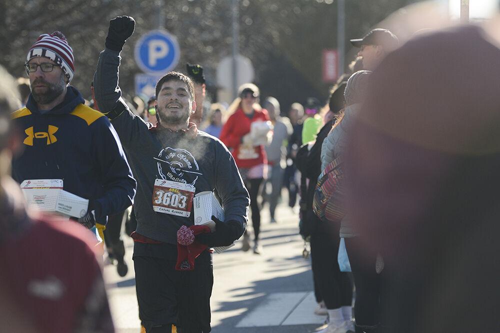 Non-challenger Abel Reynoso sticks his fist into the air in triumph after cossing the Krispy Kreme Challenge finish line on Hillsborough Street on Saturday, Feb. 4 2023. The 5 mile run was arduous, and many celebrated after crossing the finish line.