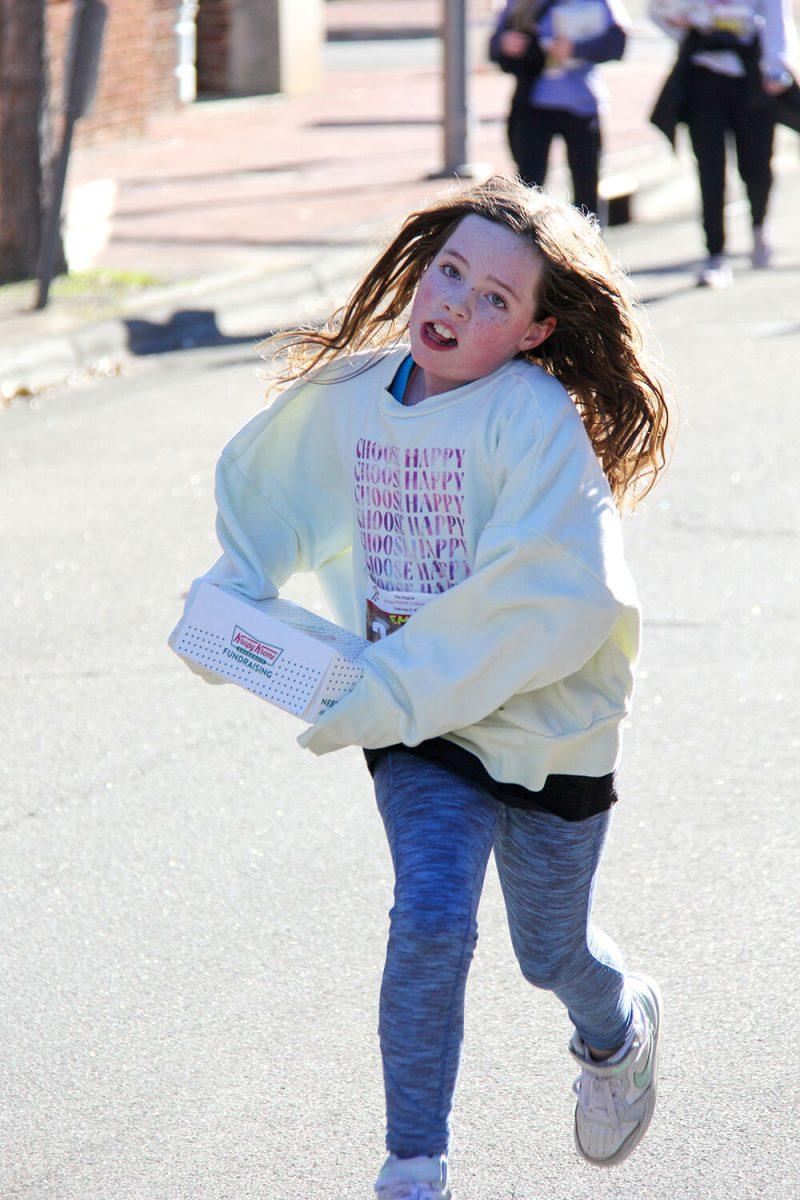 Emma Lanning runs with a box of donuts during the Krispy Kreme Challenge on Hillborough Street on Feb. 4, 2023. The challenge is an annual charity event where participants attempt to run five miles and eat a dozen donuts at the midpoint of the race, all within an hour.