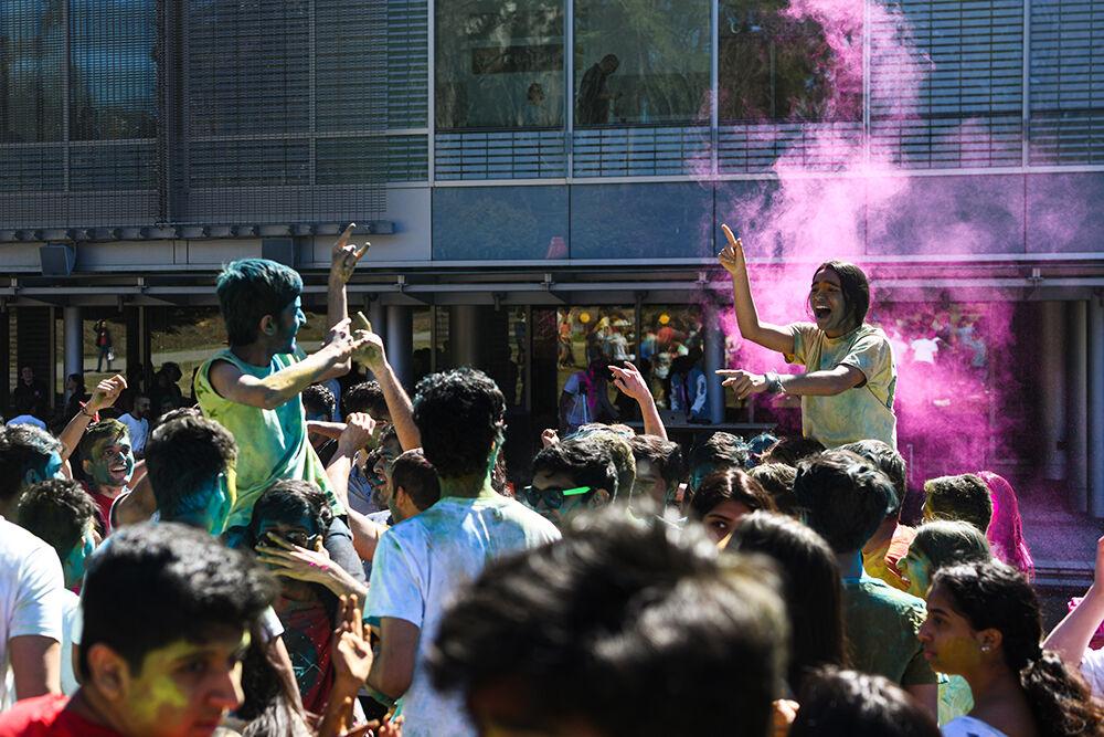 Two students ride above the crowd during the Holi celebration at Stafford Commons on Saturday, March 4, 2023. Also known as the Festival of Colors, this Hindu tradition welcomes the coming of spring and is characterized by tossing colored powder on participants.