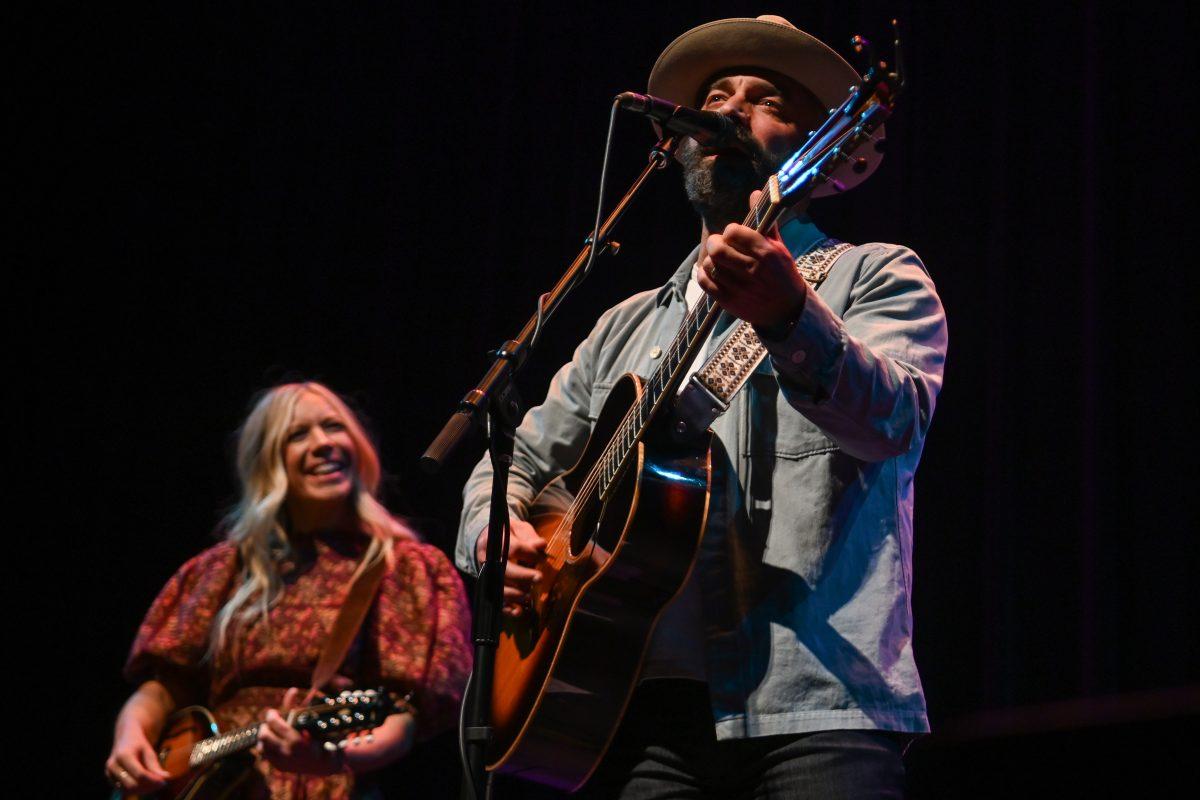 Ellie Holcomb, left, smiles at Drew Holcomb, right, while he performs during their Feels Like Home tour at The Carolina Theatre on Thursday, Feb. 15, 2024. Drew and Ellie Holcomb are a husband and wife Americana duo from Nashville, TN.