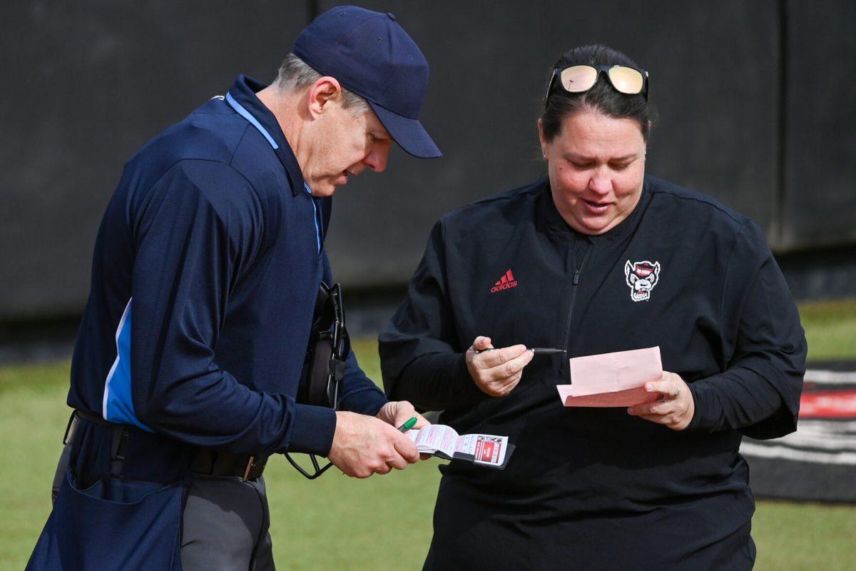 Head coach Lindsay Leftwich (right) and umpire James Cooper (left) discuss the scores during the game against Elon at Dail Softball Stadium on Saturday, Feb. 17, 2024. The Wolfpack defeated the Phoenix 5-2.