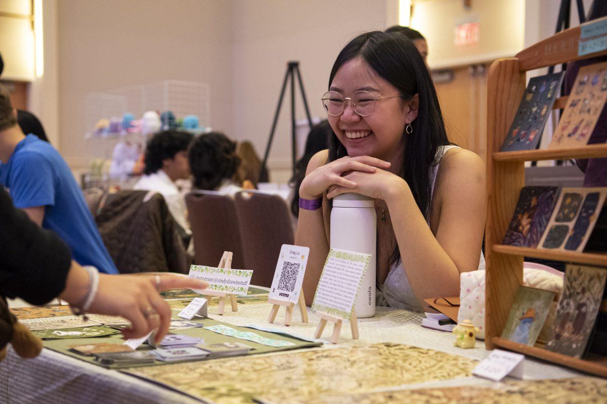 Cindy Liu, a year-one professional in veterinary medicine, smiles as visitors look through her art during the Fluorescence Asian Artist Showcase event in the Talley Ballroom on Friday, March 29, 2024. The event featured artist vendors in the Asian community as well as live performances.