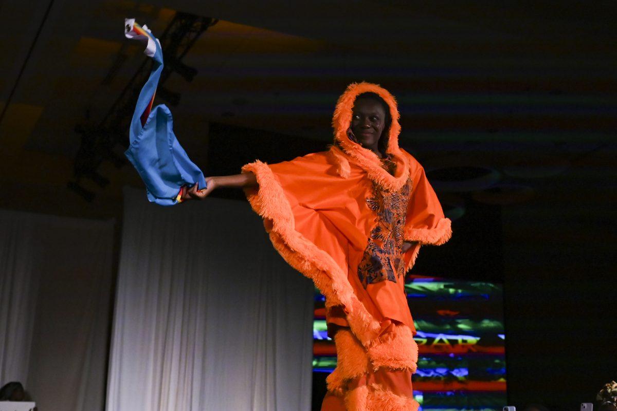 A model dances and waves a flag down the runway wearing designs from Sahara Gar's collection, "Avant-Garde," at the 26th Annual Fashion Expose in Tally Student Union on April 8, 2024. The Expose is a part of Pan-Afrikan Week and was hosted by the African American Textile Society.