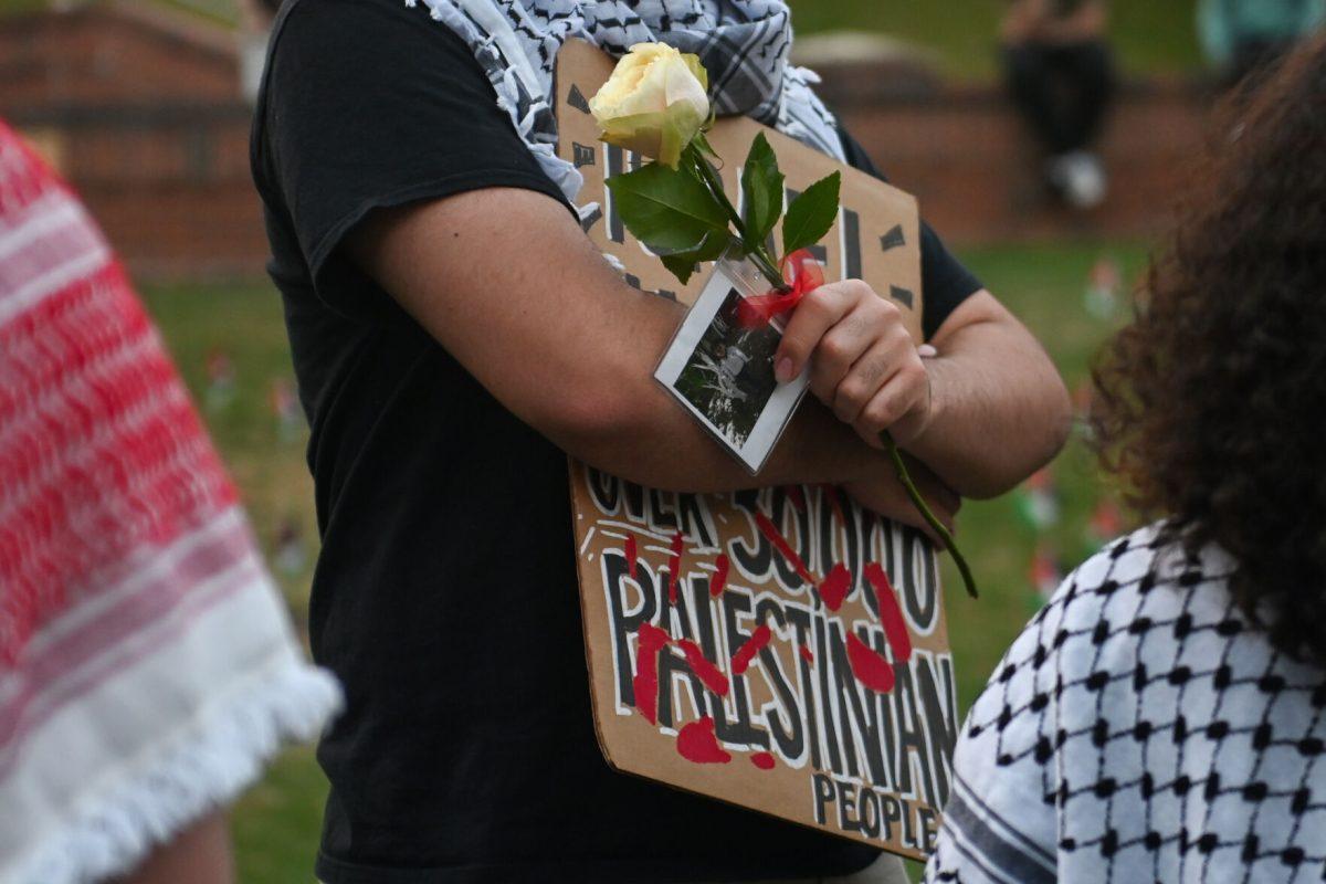 A participant stands holding a sign and a rose with a photo of a deceased Gaza resident during the vigil for Gaza at the Court of the Carolinas on Friday, April 19, 2024. The vigil event was organized by NC State's chapter of Students for Justice in Palestine as a part of Palestine Solidarity Week.&#160;