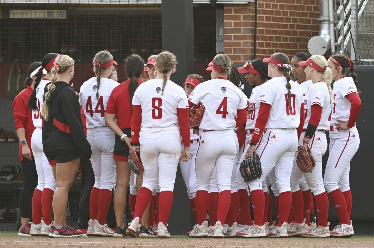 The softball team gathers near the home dugout for a mid game talk with the coach during the gam against Duke at Dail Softball Field on April 26, 2024. NC State lost to Duke 4-3.