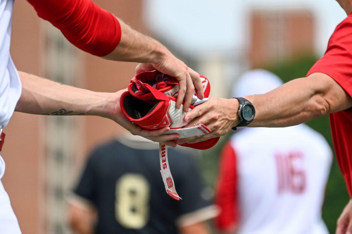 Assistant coach Bo Robinson hands off the protective guards of the runner on first base to junior pitcher Win Scott during the game against Wake Forest at Doak Field at Dail Park on Saturday, May 18, 2024. NC State beat Wake Forest 9-6 and swept the series.