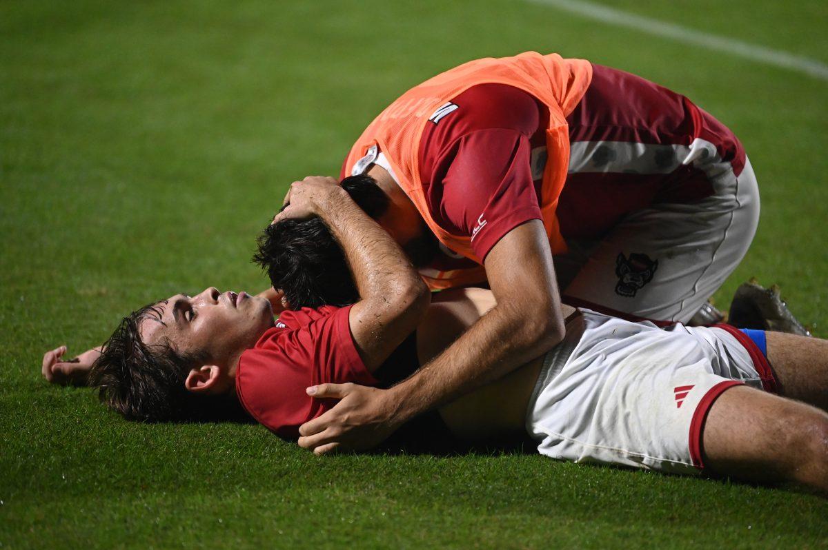 Junior center attacking midfielder Taig Healy lies on the grass and is hugged by junior forward Santiago Hoyos L&#243;pez after NC State's home ACC playoff game against Virginia at Dail Soccer Field on Wednesday, Nov. 6, 2024. The Cavaliers came from behind to defeat the Wolfpack 2-1 despite a flury of shot attempts from the Wolfpack within the last minute of the game.