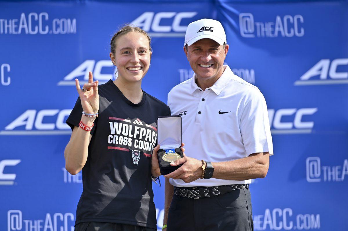 Junior runner Grace Hartman poses with ACC Commissioner James J. Phillips during the Cross Country ACC Championship at WakeMed Soccer Park on Friday, Nov. 1, 2024. Hartman finished first in the women's 6k with a time of 19:15.1. The NC State women's team finished in fifth place.