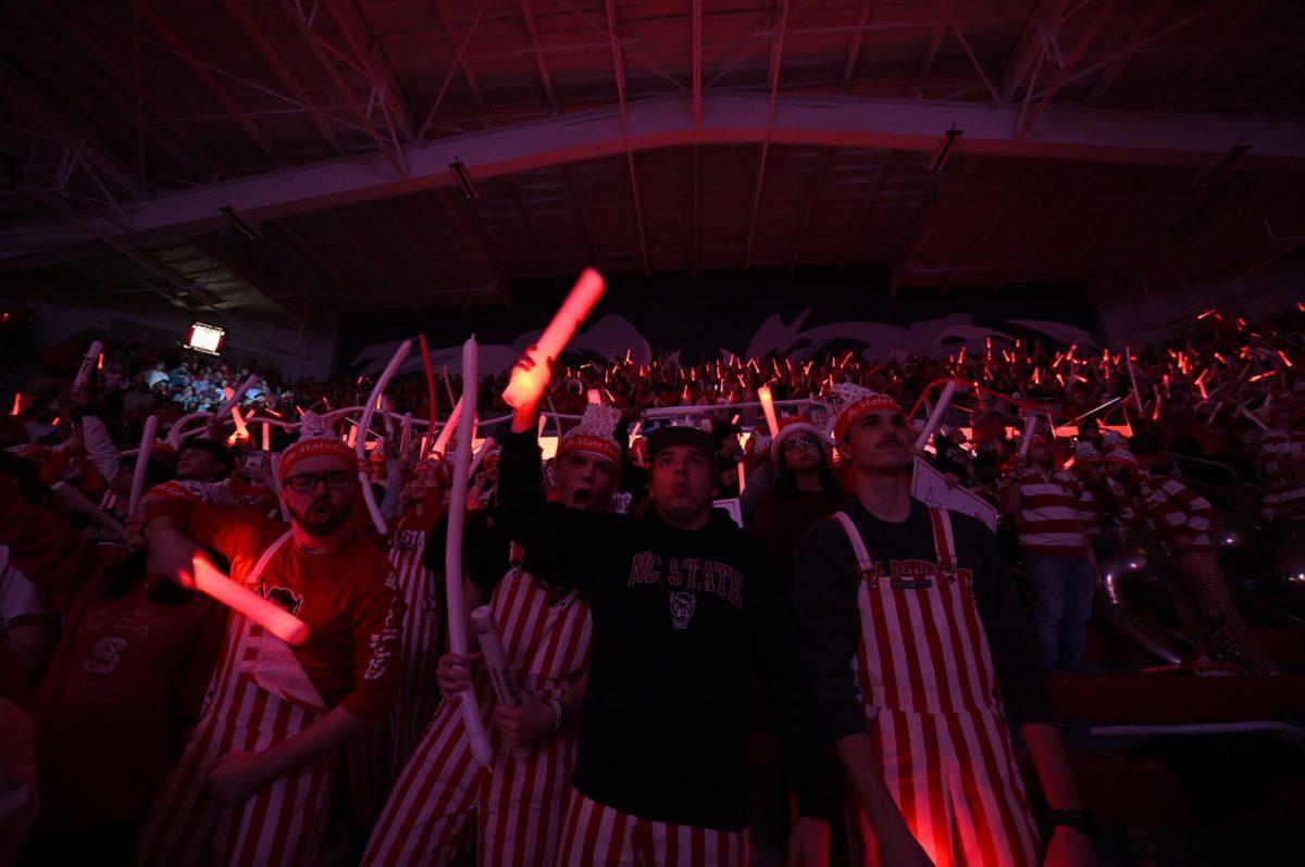 The NC State student section donn basketball net hats and hold signs and glow sticks before the start of NC State's basketball game against the Notre Dame Fighting Irish in Reynolds Coliseum on Sunday, Feb. 23, 2025. The Wolfpack beat the number one ranked Fighting Irish 104-95 in double overtime.