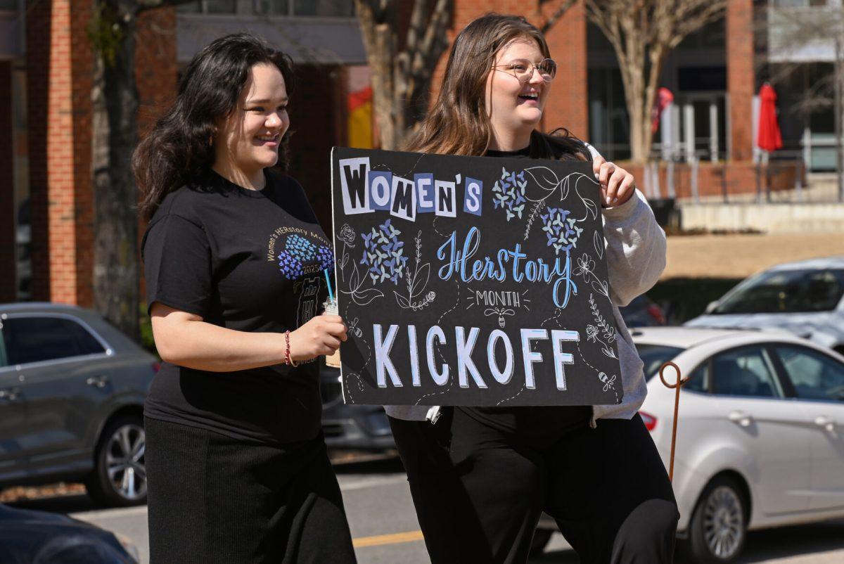 Allyson Rodriguez, a first-year studying microbiology, and Tyra Frye, a fourth-year studying English literature and women's gender and sexuality studies, carry around a colorful sign to spread awareness for the event during the Women's HERstory Month Kickoff at The Corner on Centennial Campus on Friday, Feb. 28, 2025. The event was an opportunity for students to learn about the Women's Center's upcoming programs, collect essentials like lotion and hand sanitizer, and make crafts.