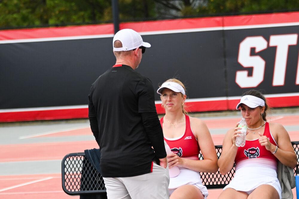 Head coach Simon Earnshaw talks with sophomores Maddy Zampardo and Gabriella Broadfoot during their doubles match against Georgia Tech at J.W. Isenhour Tennis Center on Sunday, March 30, 2025. Zampardo and Broadfoot won their doubles match 6-2. The Wolfpack beat the Yellow Jackets 4-3.