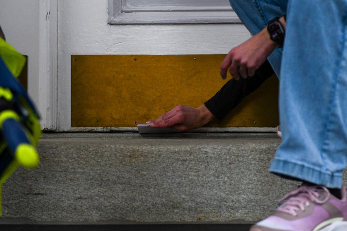 A demonstrator slides a petition letter under the front door of Holladay Hall during the Free Mahmoud rally on Thursday, March 20th, 2025. The hall's front door was locked, so demonstrators delivered their letters through alternate means.