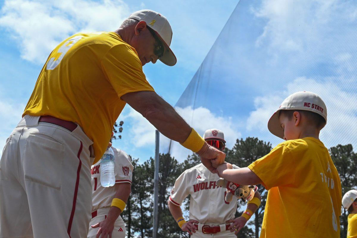 Head coach Elliot Avent gives a cancer survivor a fistbump before the game against Clemson at Doak Field at Dail Park on Saturday, April 26, 2025. NC State raised $17,465 for the V Foundation. NC State beat Clemson 4-1.