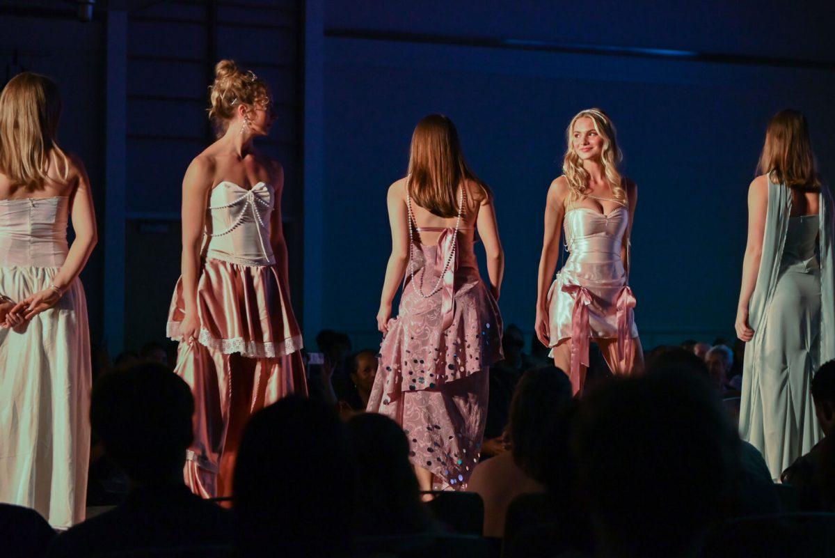 Two models look at each other while posing one last time in "Pearls in Bloom," a collection designed by Sarah Grace Simas, a second-year studying fashion and textile design, during the 27th Annual Fashion Expose at Talley Student Union on Thursday, April 10, 2025. The event featured works from student designers at various skill levels, novice, intermediate and beyond.