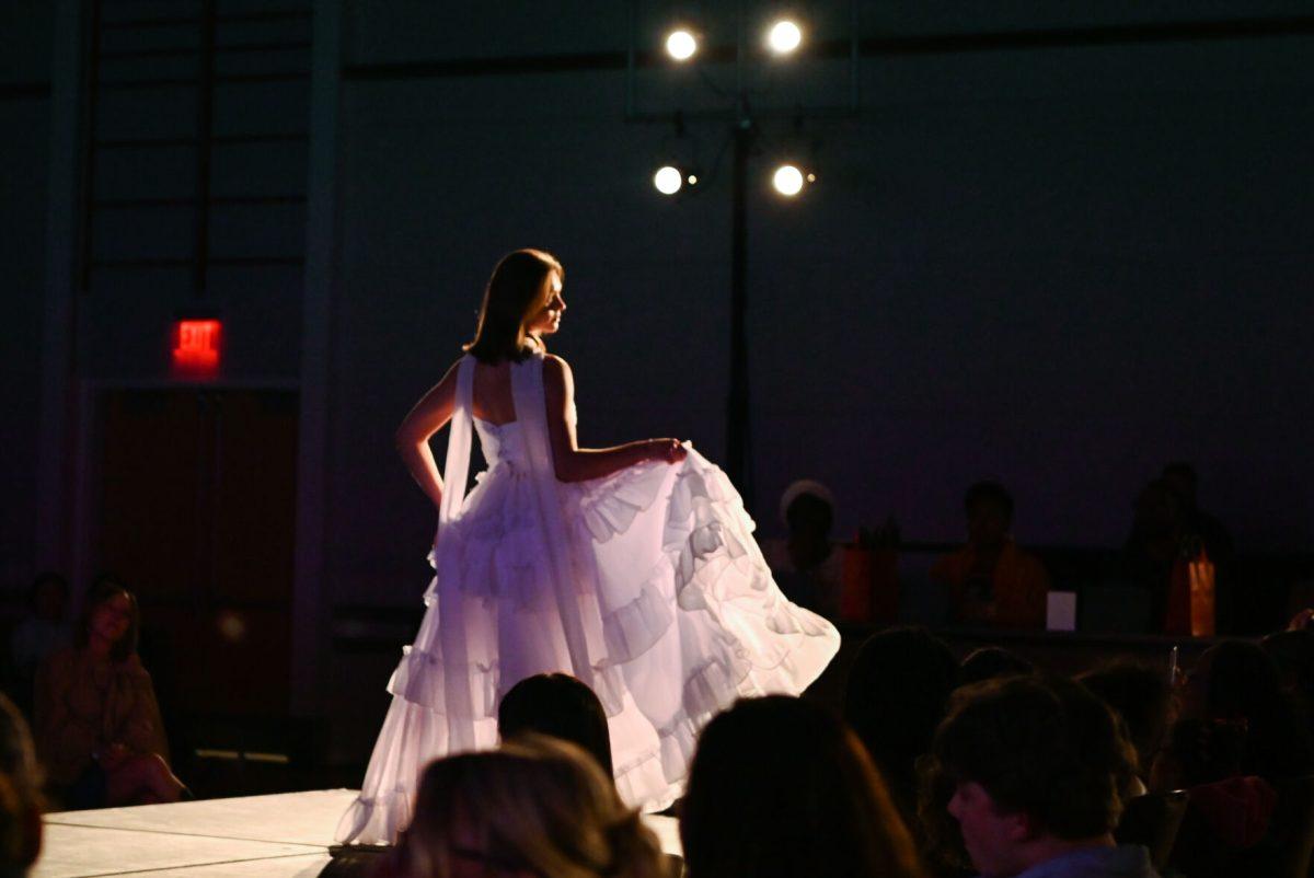 Posing in front of a panel of judges, a model lifts the skirt of a dress designed by Grace Chen, a second-year studying fashion and textile design, as part of her collection, "In the Midst Of," during the 27th Annual Fashion Expose at Talley Student Union on Thursday, April 10, 2025. Chen was a designer who competed in the intermediate and beyond category of the fashion expose.