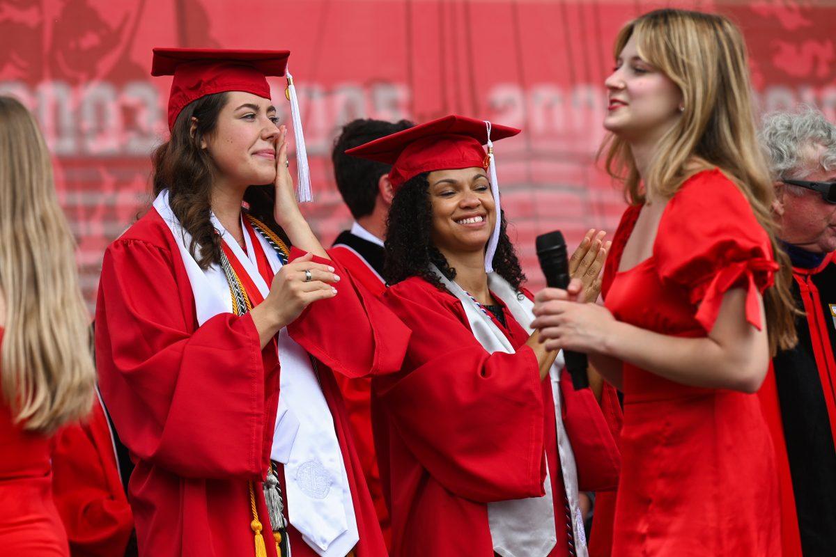 Allison Markert, graduating with a bachelor's in natural resources with a concentration in policy and administration, and Terrica Lewis, graduating with a bachelor's of arts in communication, respond to a performance by the Ladies in Red, including Katie Tohill, a second-year studying communication and art studies, as they leave the stage during the Spring Commencement Ceremony at Carter-Finley Stadium on May 3, 2025. Markert, the student body president, and Lewis, the student speaker for the spring 2025 graduating class, sat next to each other during the ceremony.